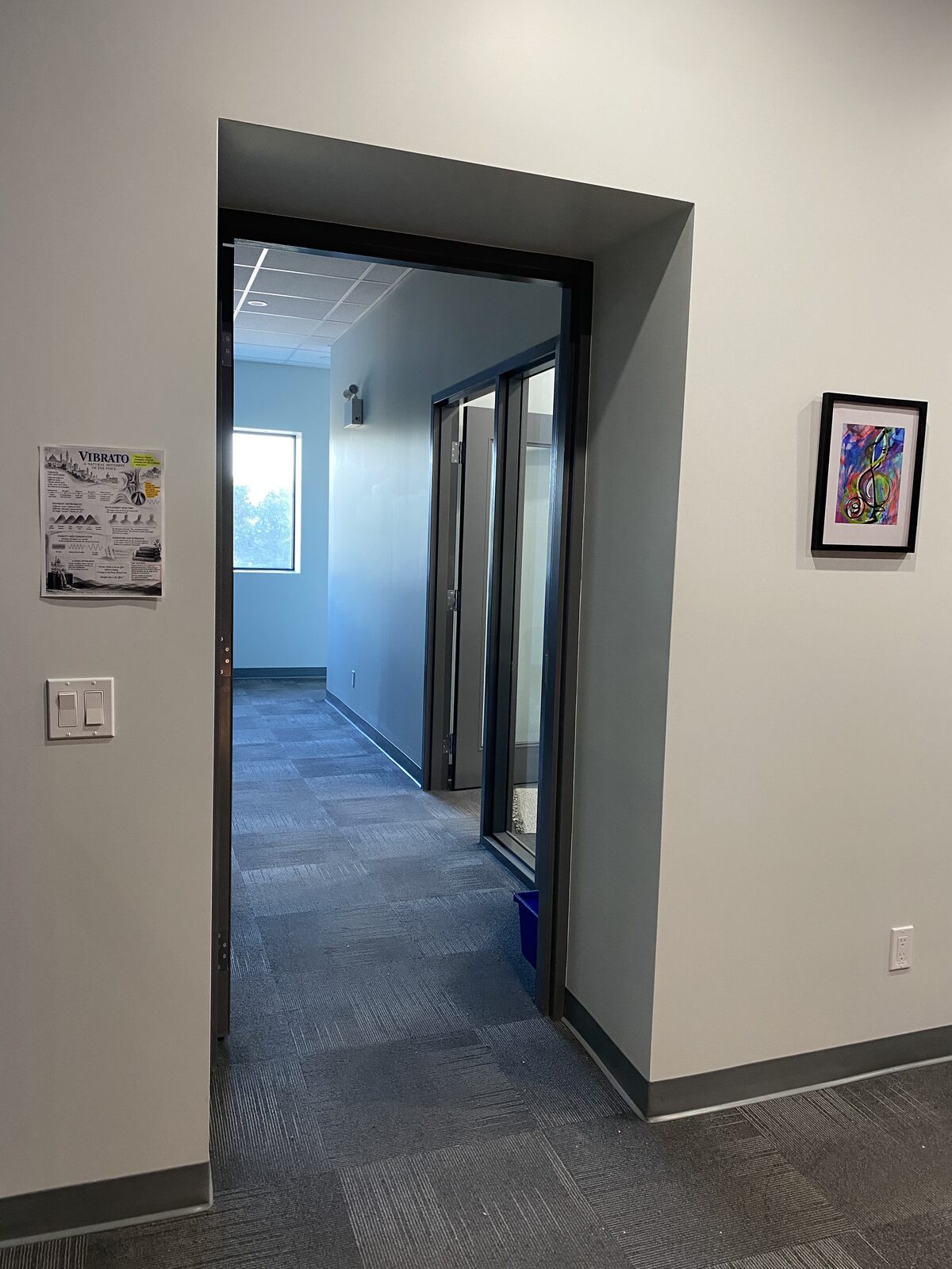The hallway to the teaching room, with a framed treble-clef painting and a poster about vibrato on the wall.