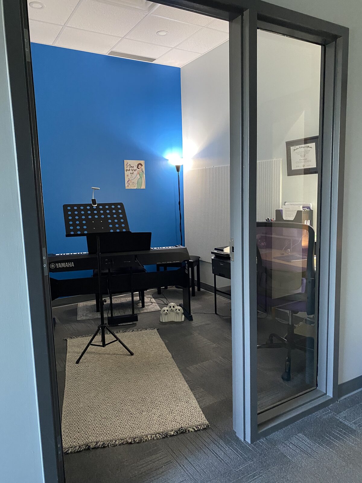 The teaching room: a Yamaha digital piano and a music stand in front of a bright blue wall.