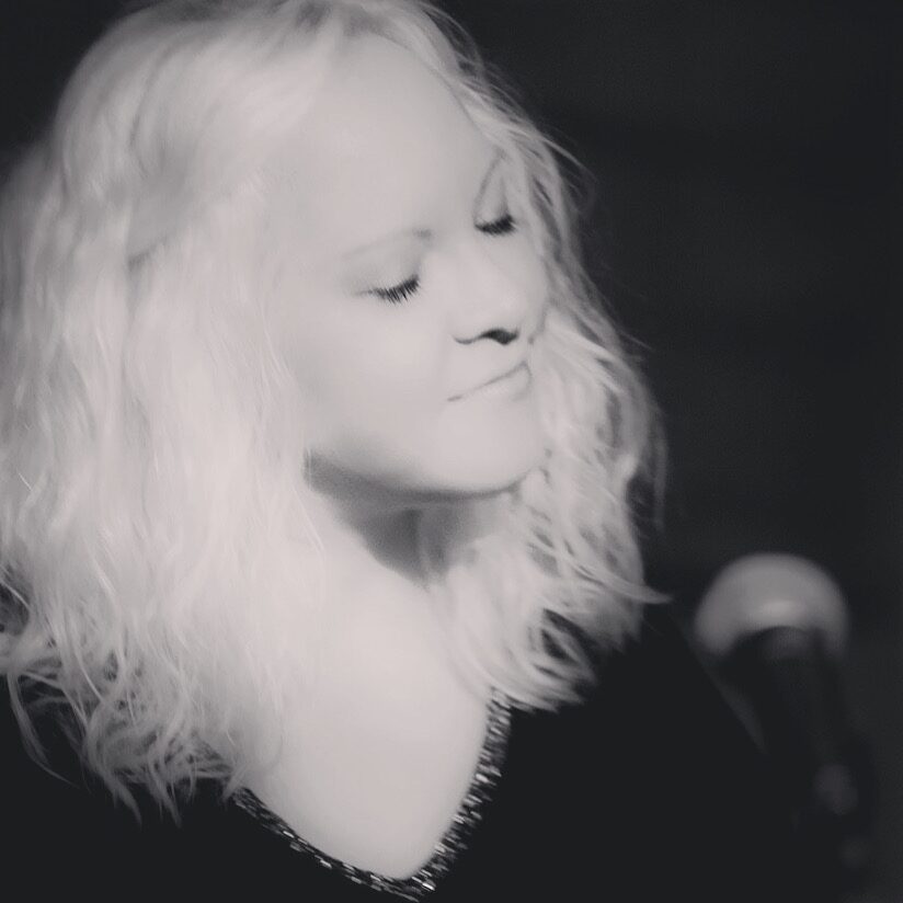 Katie Smith singing at a microphone, eyes closed, in black and white.