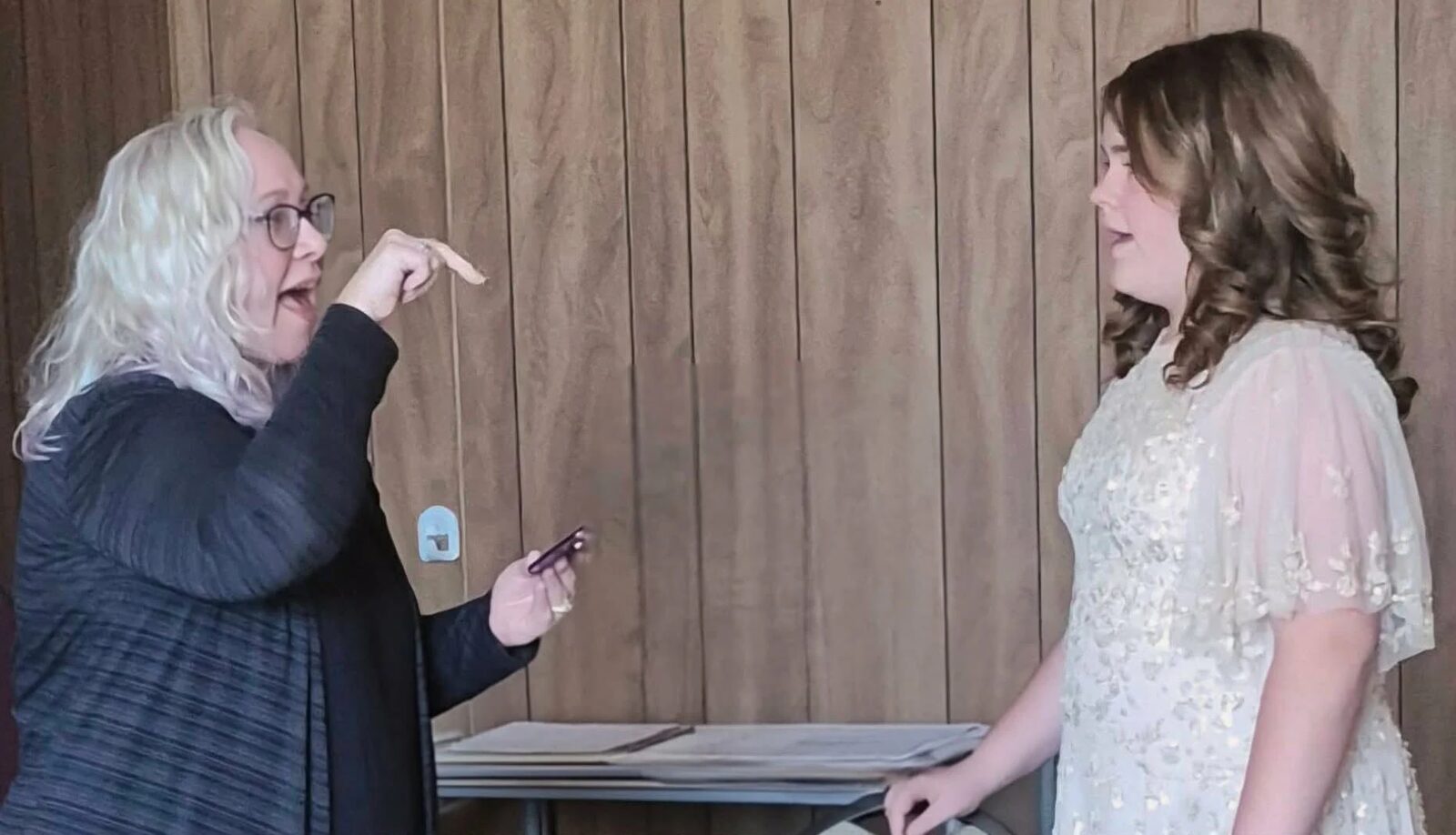 Katie, gesturing as she coaches, warms up a young singer in a lace dress before a competition.